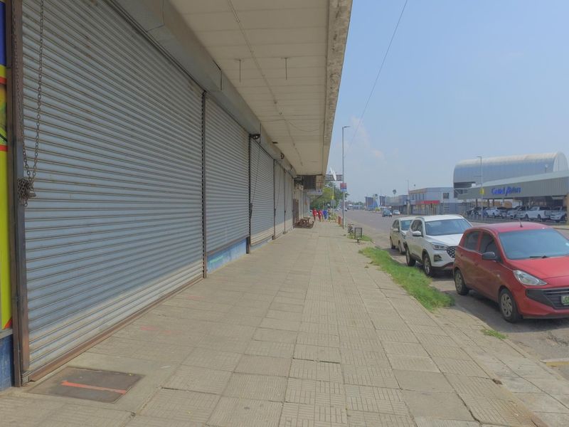 Exterior view of a retail property featuring a covered walkway and multiple roller shutter doors along the storefront.