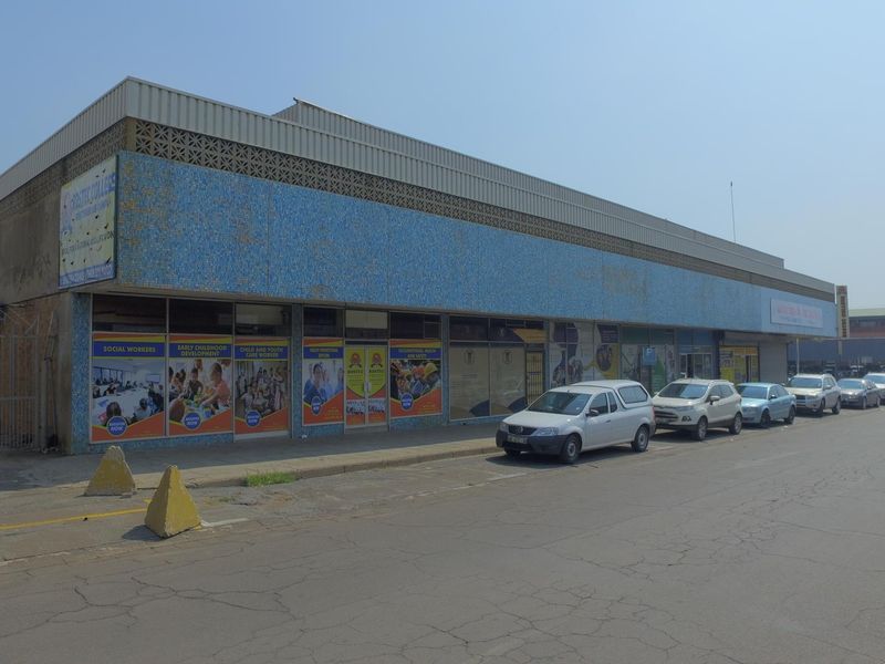 Street-level view of a commercial retail building featuring a blue mosaic tile facade, large storefront windows, and adjacent street parking.