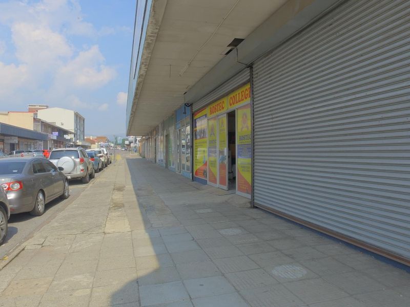 Street-level view of a retail storefront featuring roller shutter doors, a paved sidewalk, and an overhanging canopy.