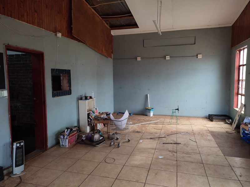 An open-plan industrial space featuring ceramic tiled flooring, exposed ceiling sections, and surface-mounted electrical conduits, requiring significant refurbishment and cosmetic repairs.