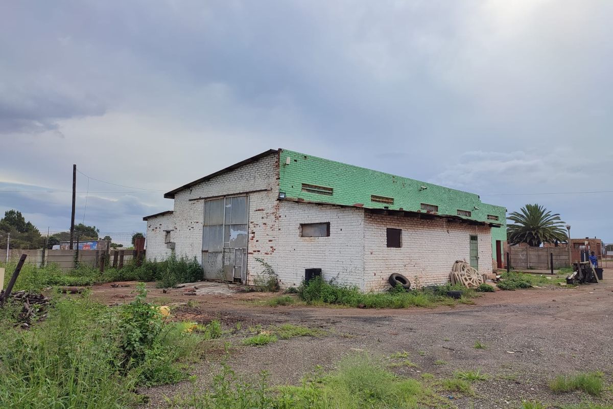 Industrial warehouse building featuring a brick facade, metal roof, and large roller door access, situated on a large plot with perimeter fencing.