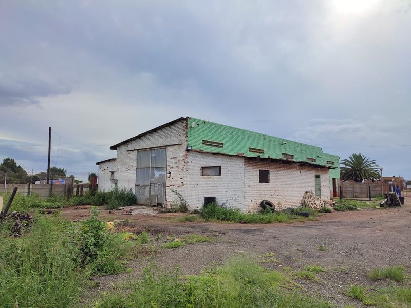 Industrial warehouse building featuring a brick facade, metal roof, and large roller door access, situated on a large plot with perimeter fencing.