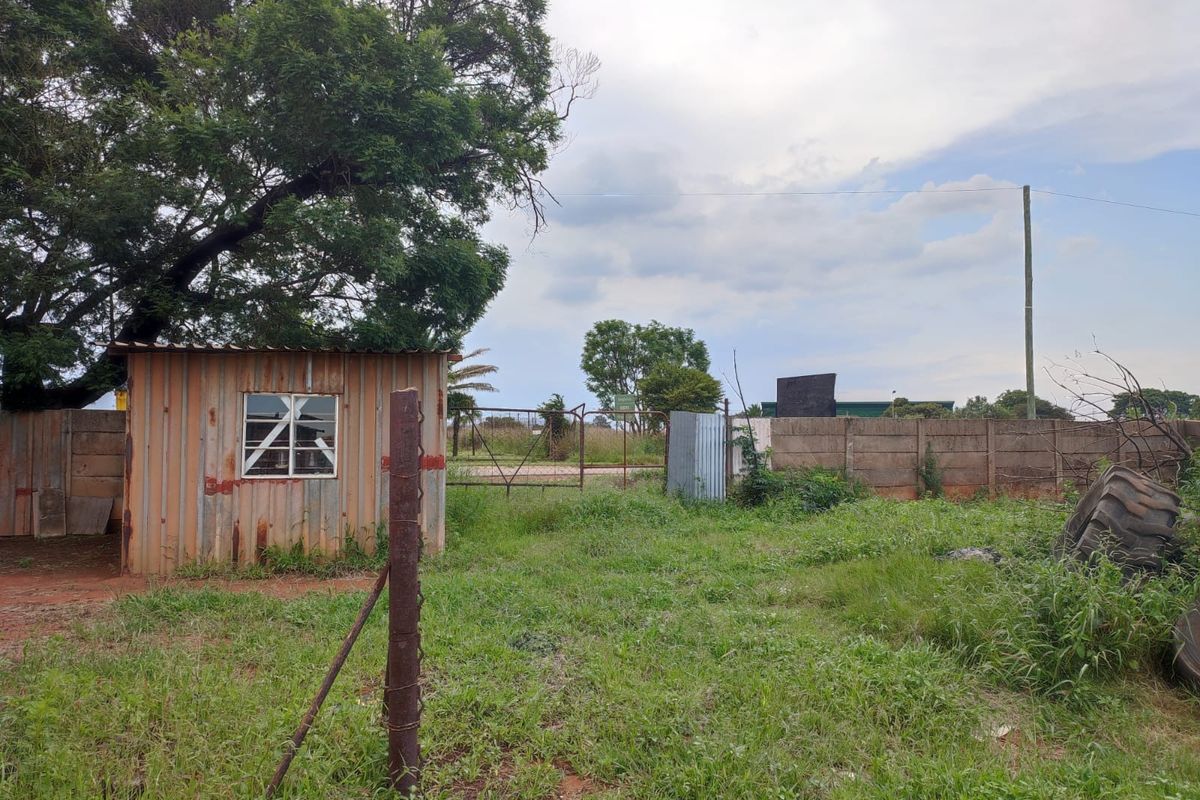 Rear exterior view of the industrial property featuring a corrugated metal structure, precast concrete boundary wall, and open yard space.