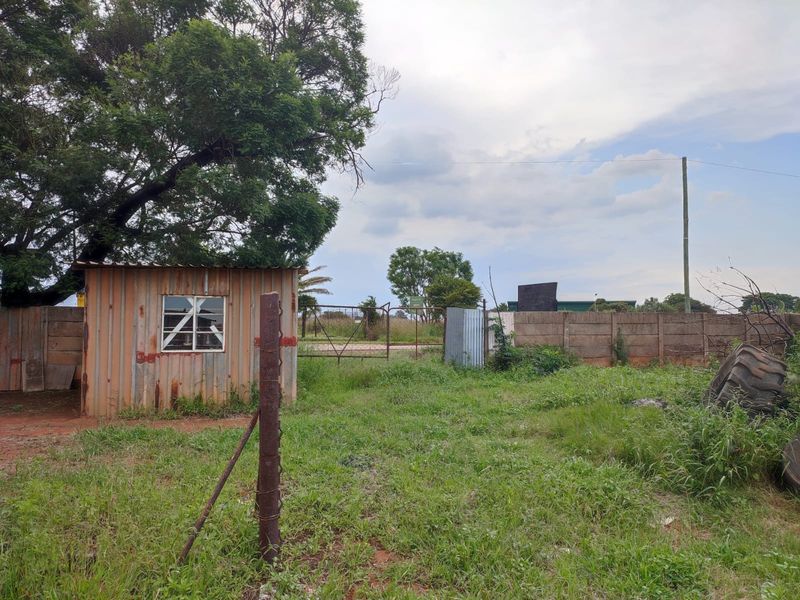 Rear exterior view of the industrial property featuring a corrugated metal structure, precast concrete boundary wall, and open yard space.