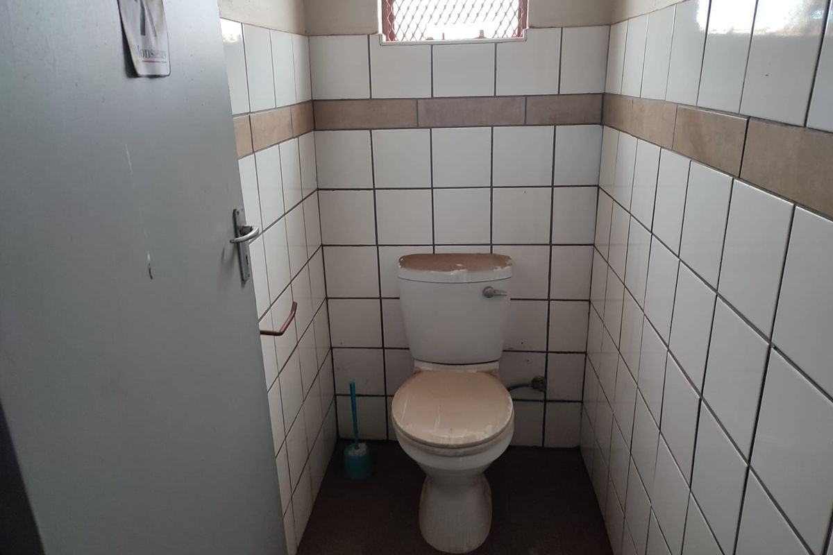 A small, functional industrial restroom featuring tiled walls and a standard ceramic toilet unit.