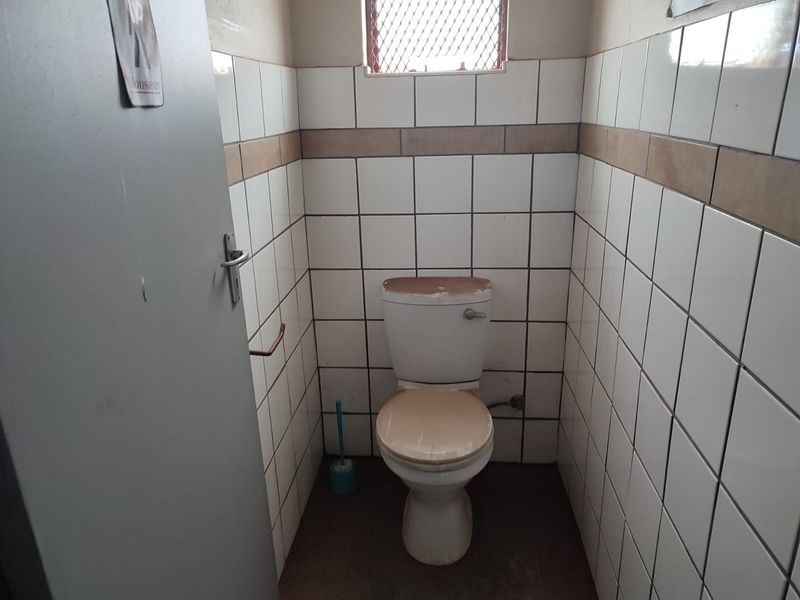 A small, functional industrial restroom featuring tiled walls and a standard ceramic toilet unit.