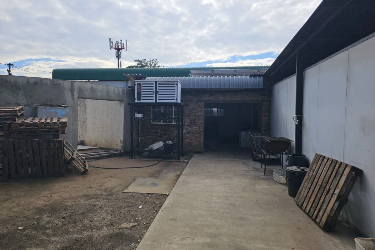 Rear exterior area featuring a concrete driveway, brick building facade, and metal roofing, suitable for industrial or commercial utility use.