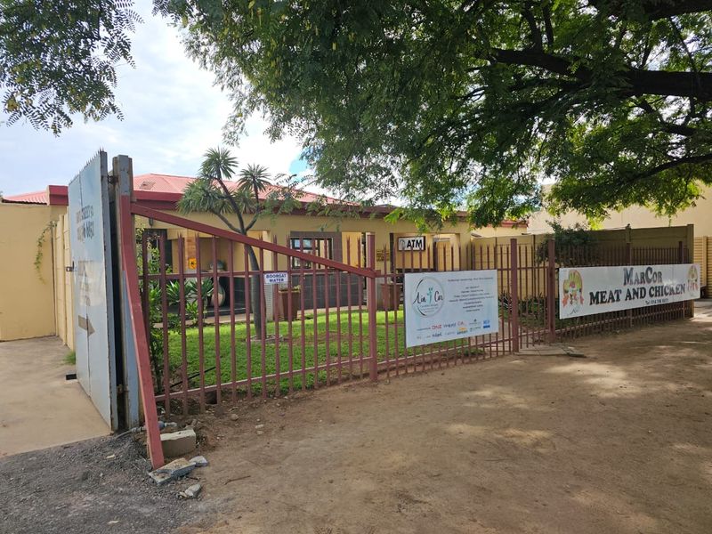Front exterior view of a commercial property featuring a metal security gate, perimeter fencing, and visible business signage.