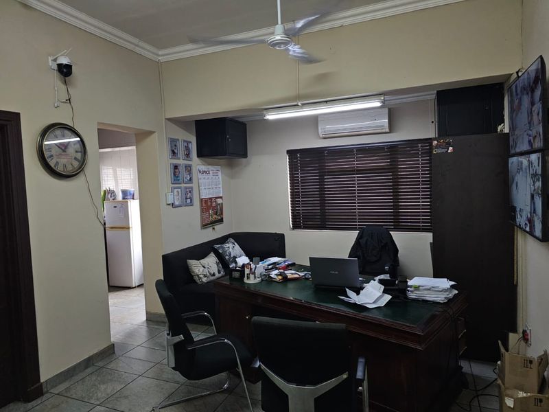 A functional office space featuring tiled flooring, a ceiling fan, split-system air conditioning, and venetian blinds, with an adjacent utility area visible.