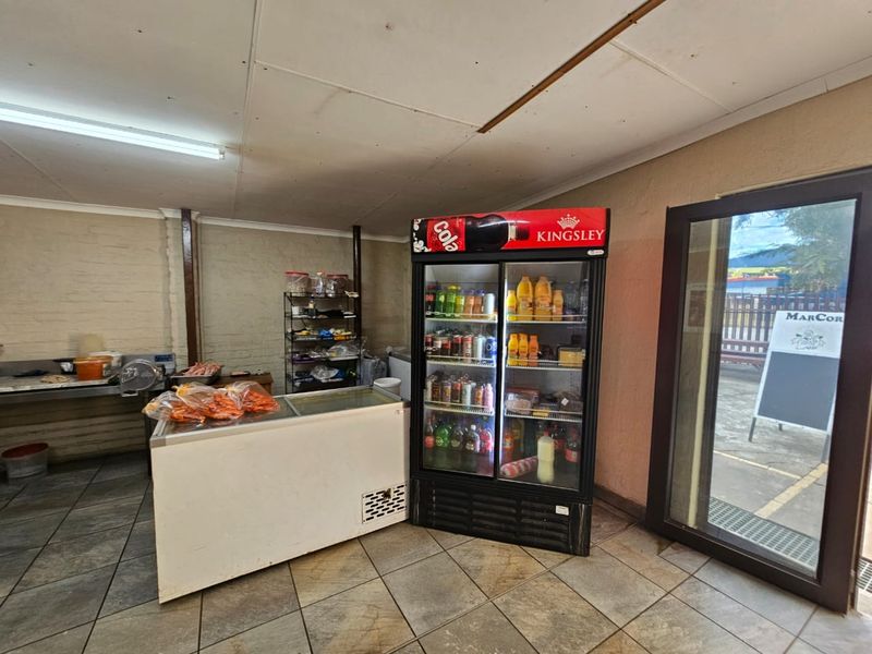 A functional utility or service area featuring tiled flooring, fluorescent lighting, and direct access to the exterior via a glass door.