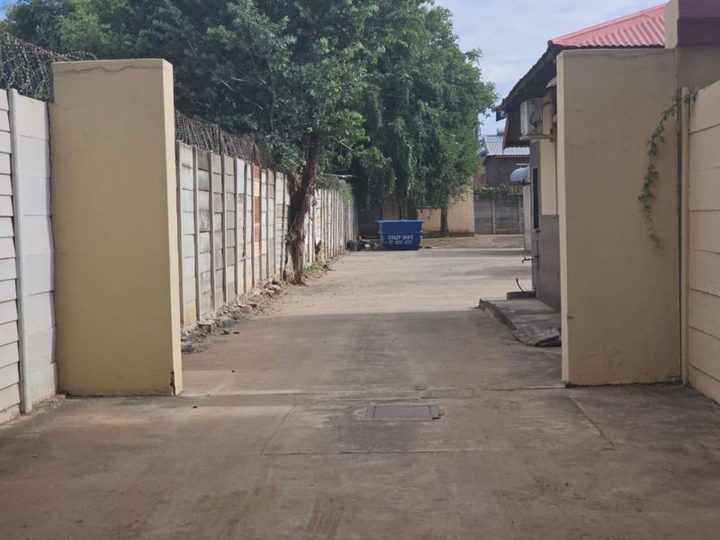 A paved driveway entrance featuring precast concrete boundary walls with security razor wire and an external air conditioning unit mounted on the building exterior.