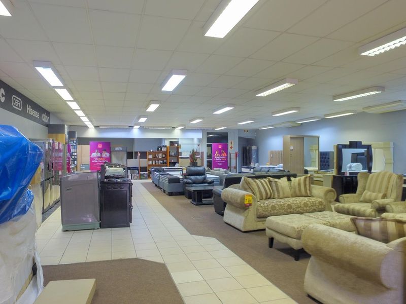 Spacious retail showroom floor featuring a combination of tiled and carpeted flooring with suspended ceiling and integrated fluorescent lighting.