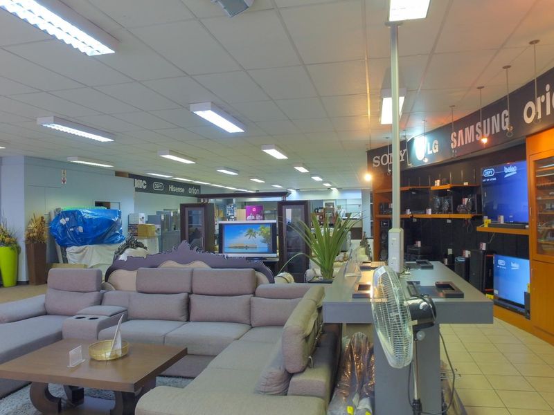 Spacious retail showroom featuring suspended ceilings, tiled flooring, and integrated wall-mounted display shelving for electronics and home appliances.