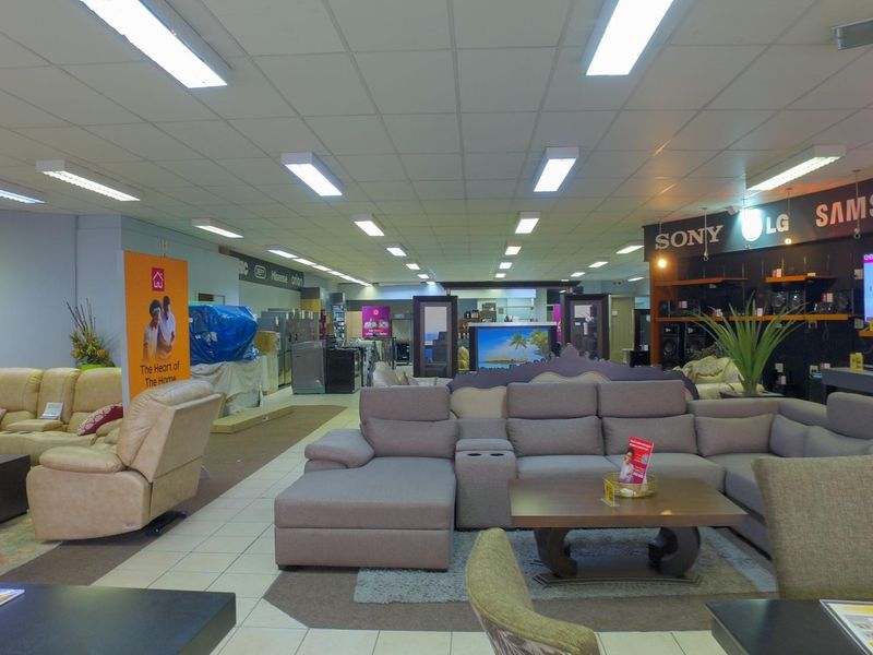 Spacious retail showroom floor featuring suspended ceilings, bright fluorescent lighting, and tiled flooring, currently configured for furniture and electronics display.