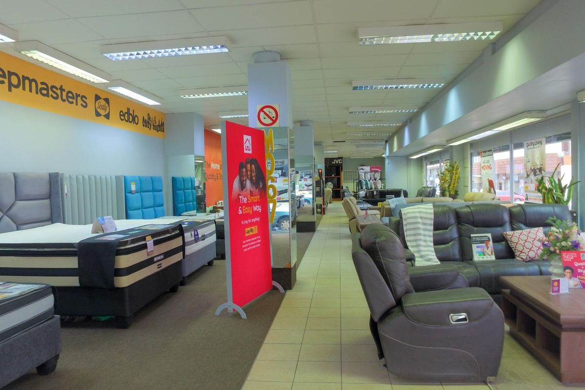 Spacious retail showroom floor featuring a mix of carpeted and tiled flooring, structural columns, and integrated fluorescent lighting throughout the commercial space.