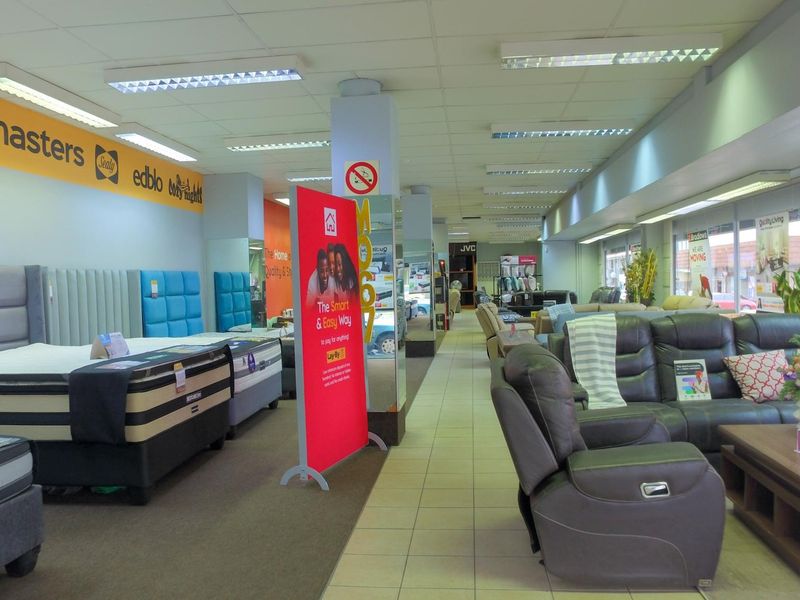 Spacious retail showroom floor featuring a mix of carpeted and tiled flooring, structural columns, and integrated fluorescent lighting throughout the commercial space.