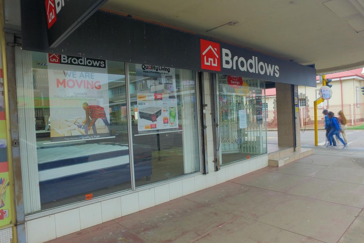 Street-level retail storefront featuring large display windows, prominent signage, and a covered walkway entrance in a commercial area.