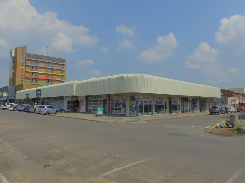 A corner retail property featuring a prominent metal awning and multiple glass storefronts, situated in a commercial street setting with adjacent parking.