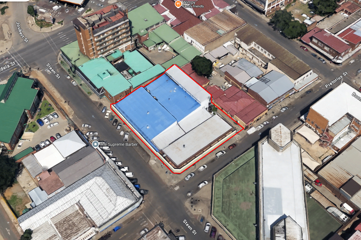 Aerial view of a commercial property block highlighted in red, featuring a large metal roof structure situated in a busy urban street intersection.