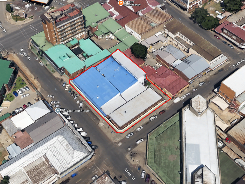 Aerial view of a commercial property block highlighted in red, featuring a large metal roof structure situated in a busy urban street intersection.