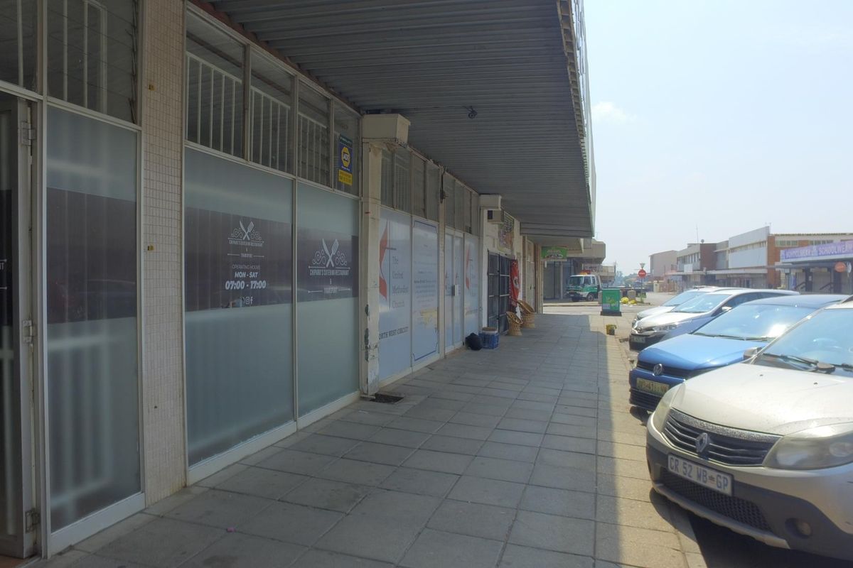 Front exterior view of a retail storefront featuring large glass windows, a covered walkway, and paved frontage in a commercial street setting.
