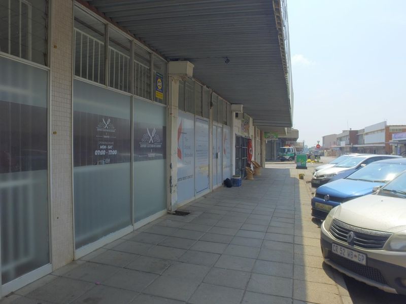 Front exterior view of a retail storefront featuring large glass windows, a covered walkway, and paved frontage in a commercial street setting.
