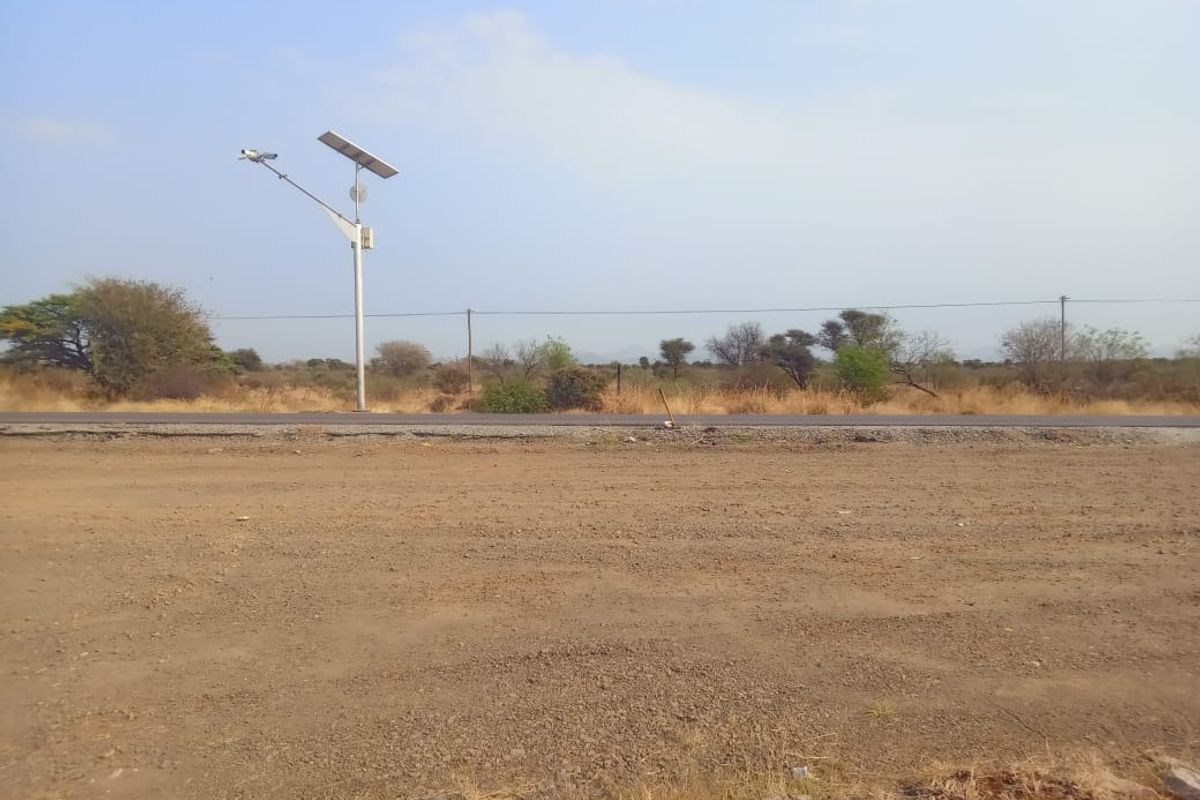 A view of the vacant commercial land featuring a gravel surface, adjacent asphalt road, and a solar-powered street light.