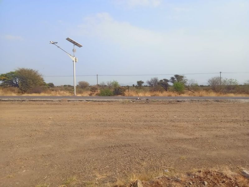 A view of the vacant commercial land featuring a gravel surface, adjacent asphalt road, and a solar-powered street light.