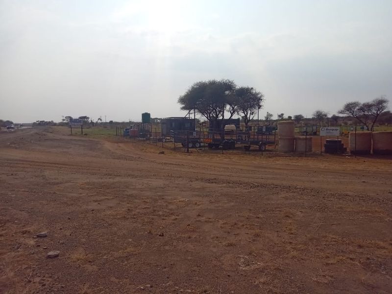 A view of the vacant commercial land featuring an unpaved access road, perimeter fencing, and a water storage tank on site.
