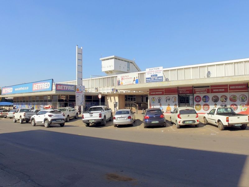 Front exterior view of a retail shopping center featuring multiple storefronts, signage, and an adjacent parking area.