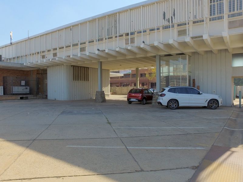 Front exterior view of a retail property featuring a paved parking area, covered structural overhang, and metal facade cladding.