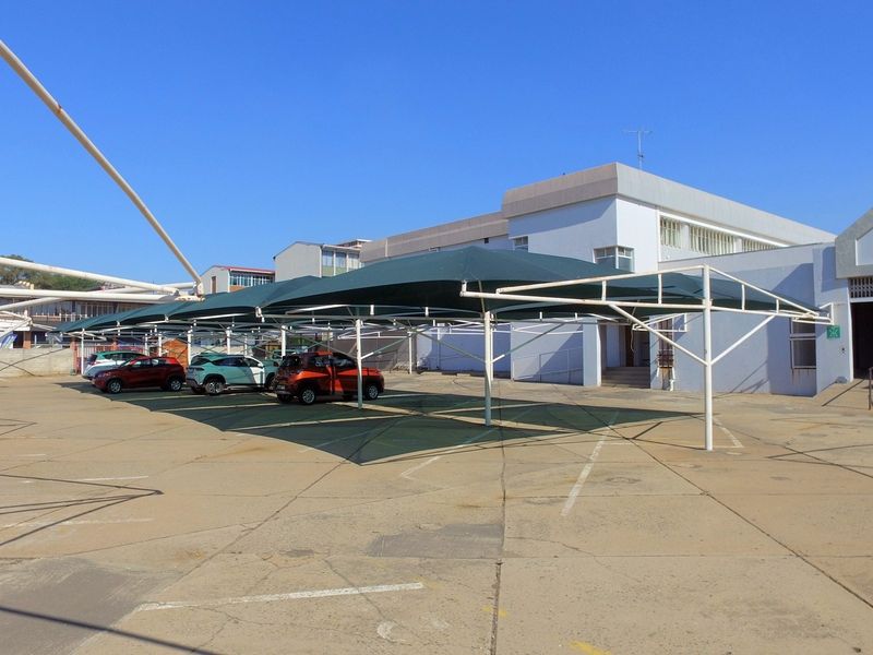 Exterior view of a retail property featuring a large paved parking area with installed shade cloth carports and a painted masonry building facade.