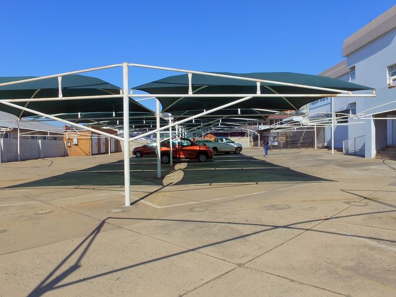 A paved outdoor parking area featuring a large shade cloth carport structure and perimeter boundary walls.