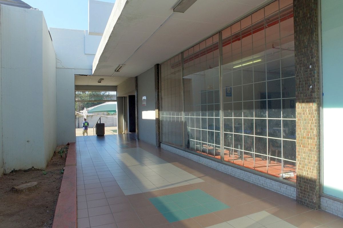 A covered exterior walkway featuring tiled flooring and large glass storefront windows, providing access to the retail space.