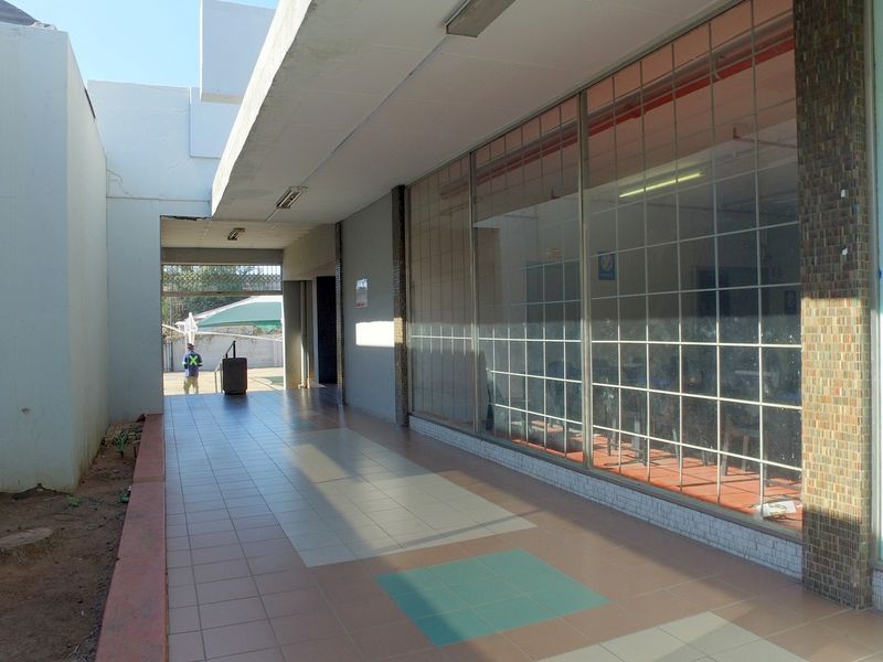 A covered exterior walkway featuring tiled flooring and large glass storefront windows, providing access to the retail space.