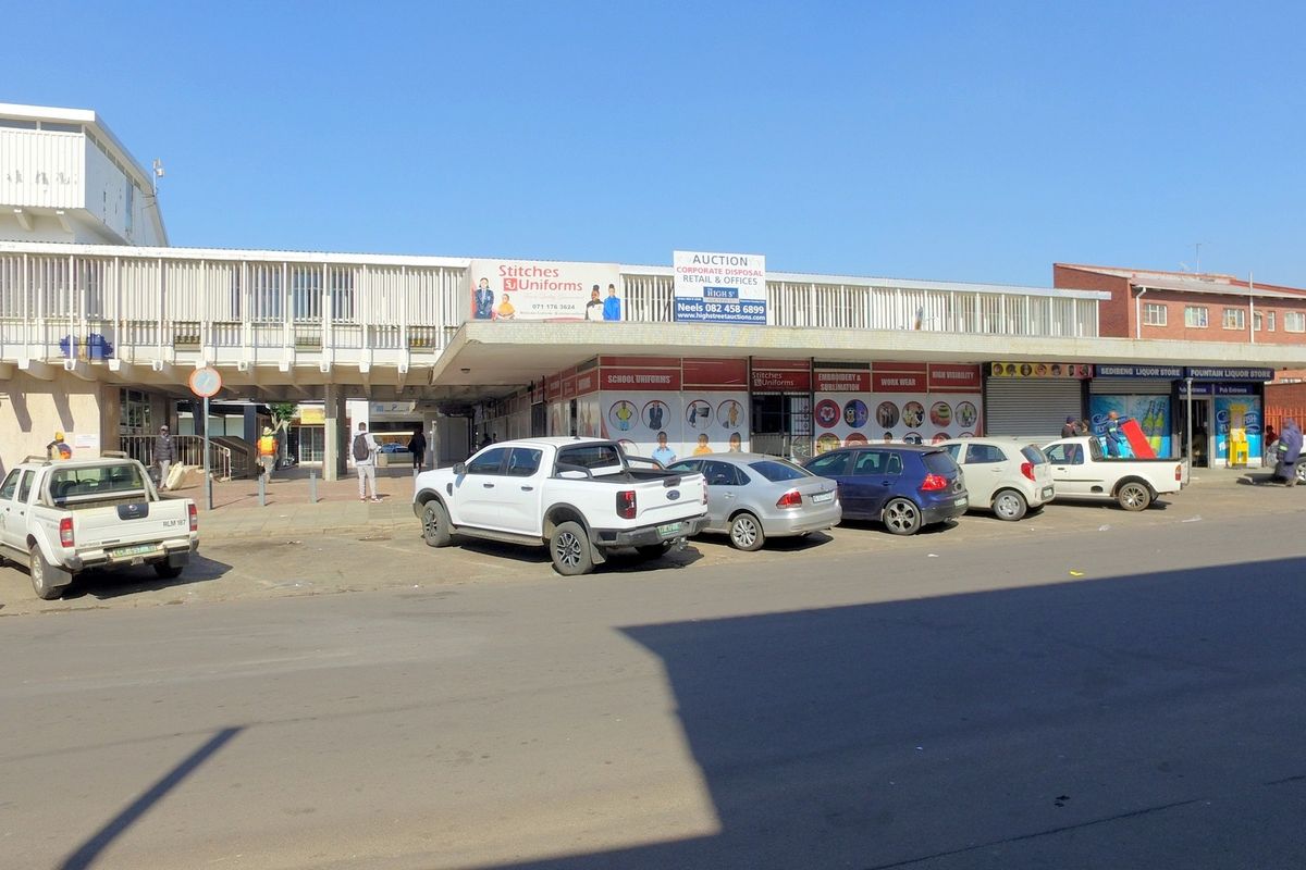 Front elevation of a retail commercial building featuring multiple storefronts, a covered walkway, and street-level parking access.