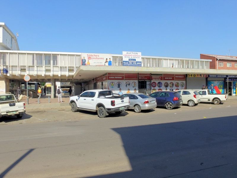 Front elevation of a retail commercial building featuring multiple storefronts, a covered walkway, and street-level parking access.