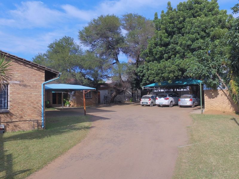 Front exterior view of the office property featuring a brick facade, paved driveway, and covered carport parking areas surrounded by established trees.