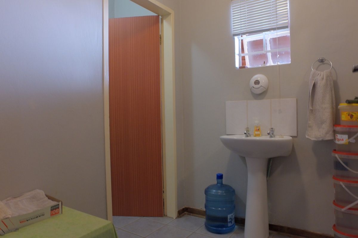 A functional office bathroom featuring a pedestal washbasin, tiled splashback, and a window with fitted blinds.
