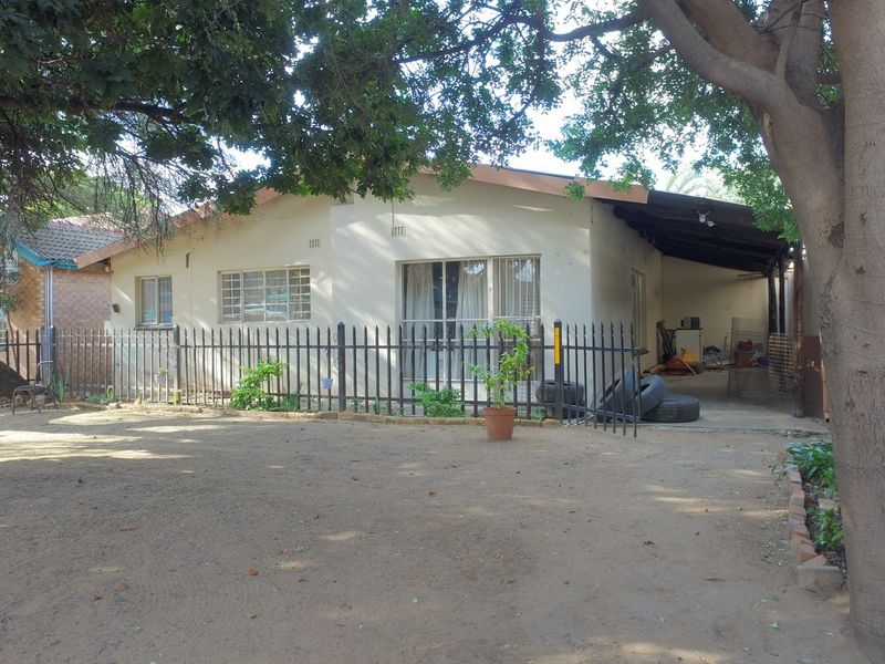 Front view of a single-story office building featuring a covered carport, metal security fencing, and a large unpaved parking area.