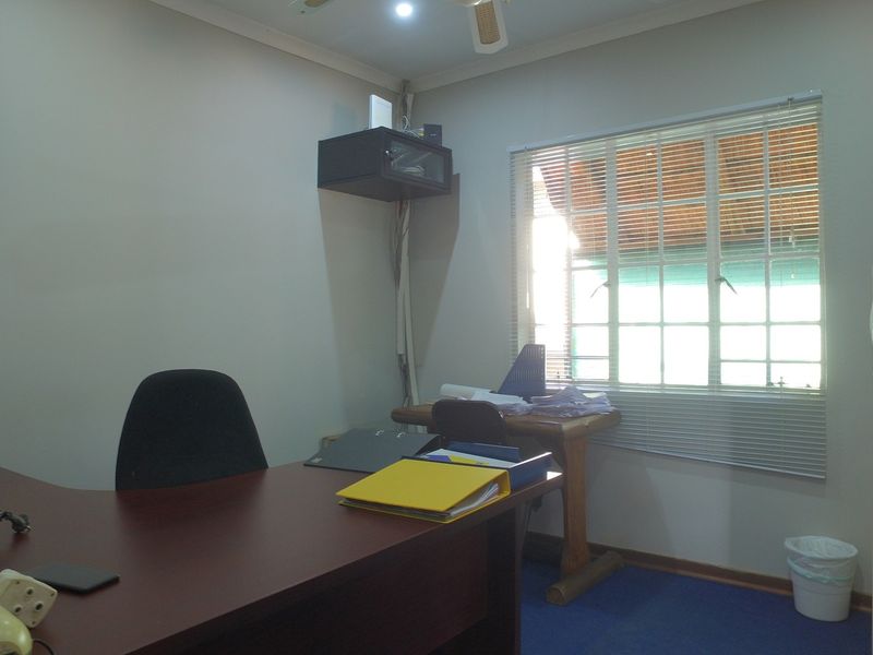 A functional office space featuring a window with fitted blinds, a ceiling fan, and a wall-mounted network cabinet.