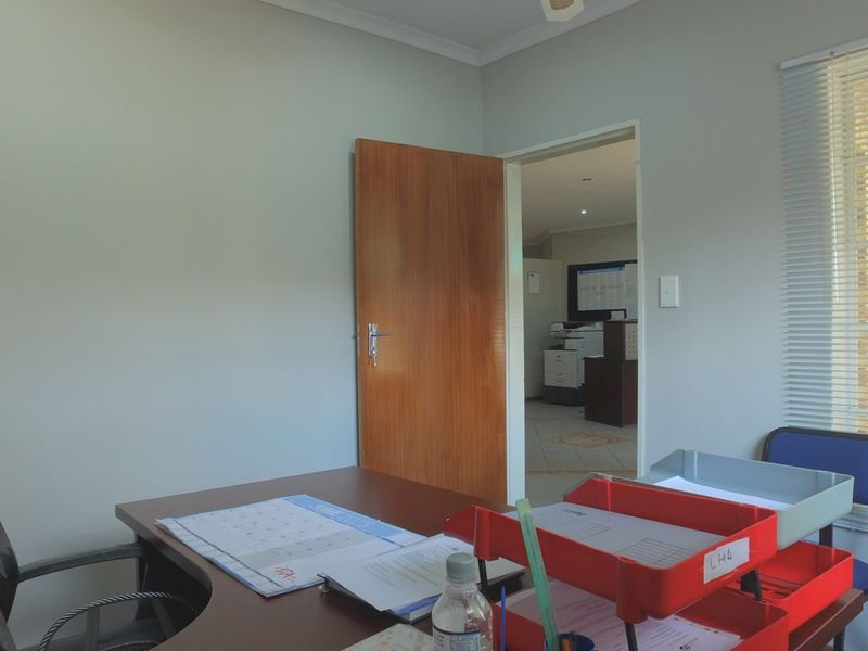 A functional office space featuring a wooden door, neutral wall finishes, and venetian blinds allowing natural light into the workspace.