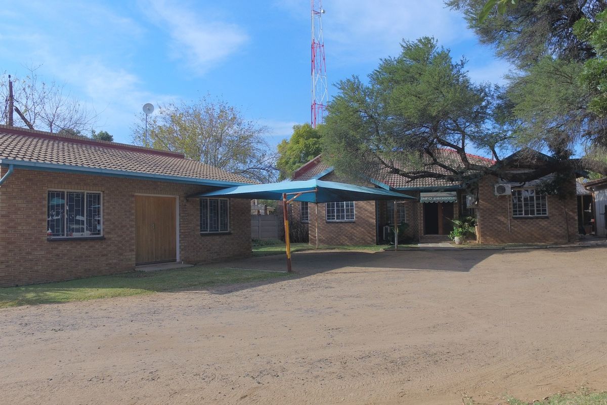 Exterior view of a brick office building featuring a shaded parking area and established trees on the property grounds.