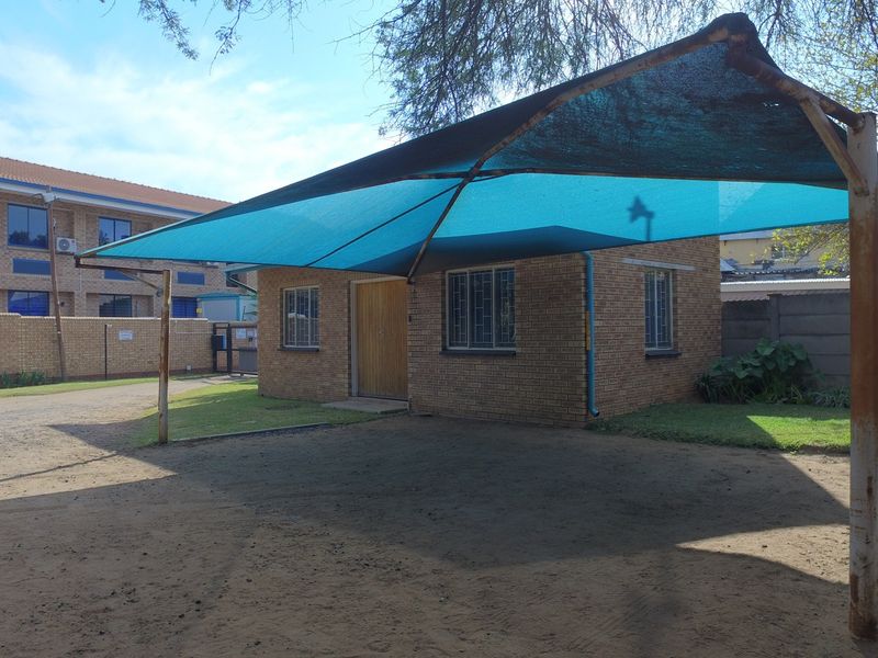 Exterior view of a facebrick office building featuring a shade cloth carport structure and surrounding garden area.