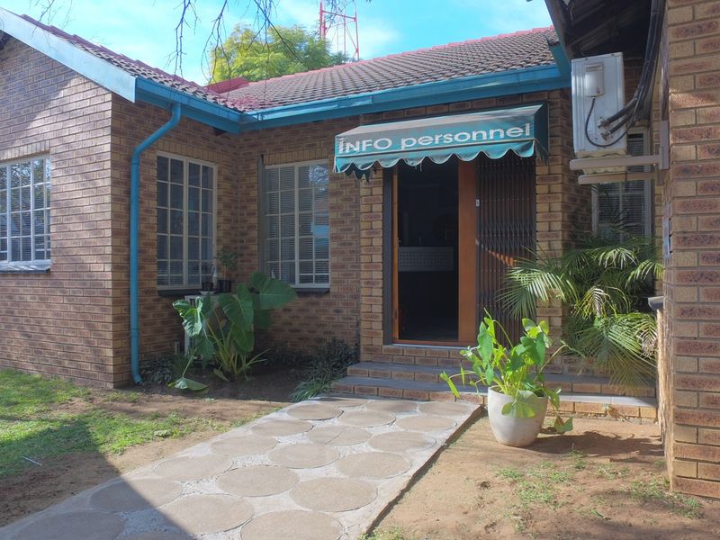 Front entrance of a face brick office building featuring a paved walkway, security gate, and external air conditioning unit.