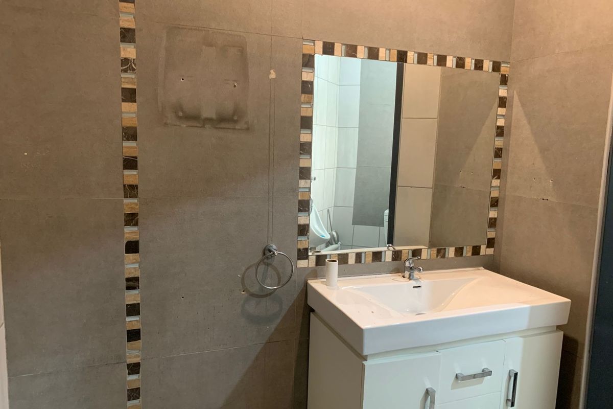 A bathroom featuring a vanity cabinet with a ceramic basin, wall-mounted mirror, and tiled walls with decorative mosaic accents.