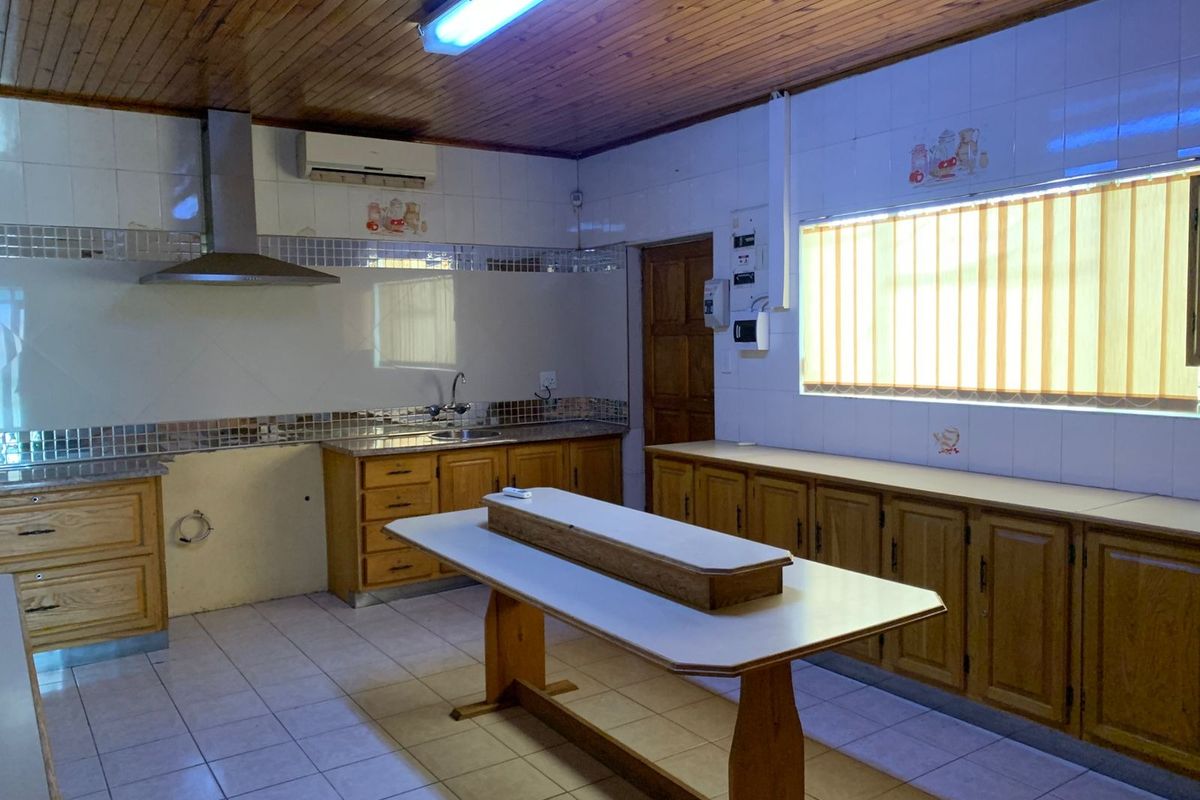 A functional kitchen featuring wooden cabinetry, tiled flooring, a stainless steel extractor fan, and a wooden ceiling, offering a dated but practical workspace.