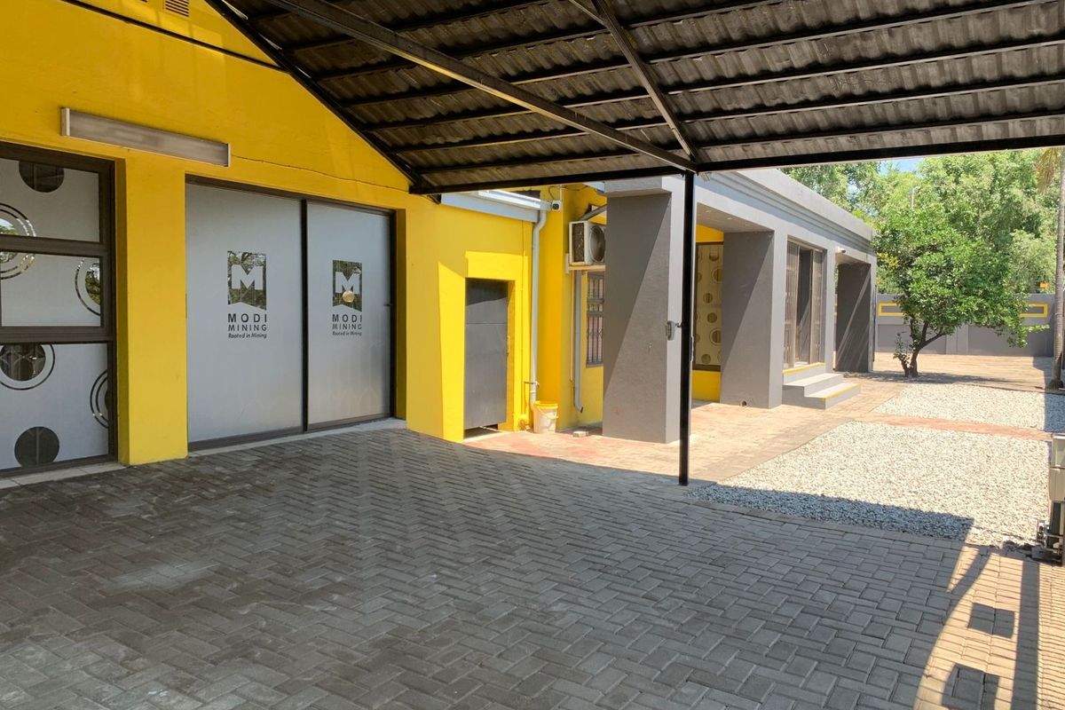 Rear exterior view of the office property featuring a paved driveway, covered carport, and modern sliding glass entrance doors.