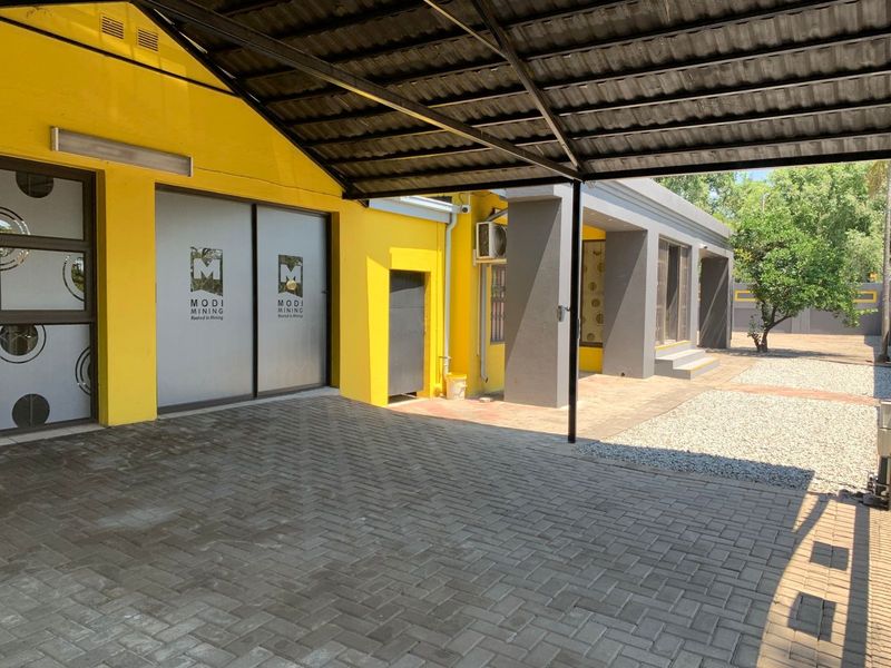 Rear exterior view of the office property featuring a paved driveway, covered carport, and modern sliding glass entrance doors.