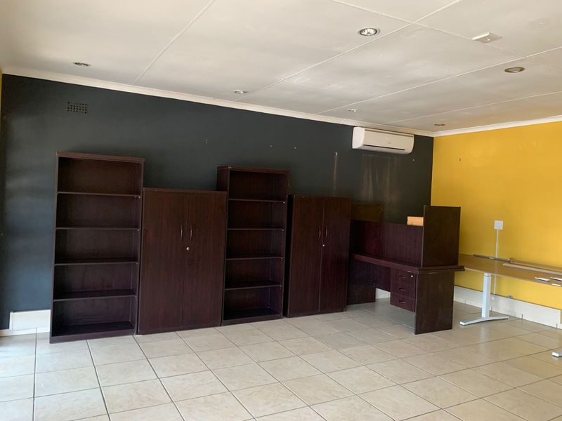 A functional office space featuring tiled flooring, recessed ceiling lighting, and a wall-mounted air conditioning unit.